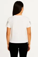 Remera blanca de algodón con cuello redondo y mangas cortas. Estampado con moños plateados brillantes.