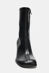 Botín de caña media en color negro, confeccionado en material sintético con acabado liso. Presenta un diseño de punta cuadrada redondeada, cierre lateral mediante cremallera y un tacón alto en bloque.