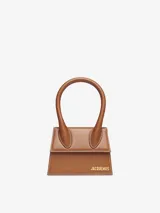 Bolso mini de cuero color marrón, con asa corta reforzada y correa larga extraíble. Cierre magnético, bolsillo interior y herrajes metálicos dorados.