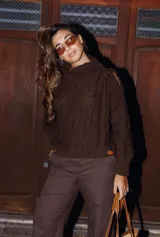 Sweater marrón de lana gruesa con cuello alto y hombros descubiertos, unidos por una tira con hebilla metálica.