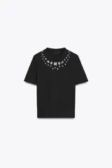 Camiseta negra de manga corta y cuello redondo, con apliques de joyas en el escote.