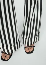 Pantalón largo de tela fluida con estampado de rayas verticales en blanco y negro. Diseño recto con bajo con vuelta, cierre oculto de botón, gancho y cremallera, y dos bolsillos laterales.