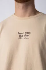Remera color beige de corte oversize, con cuello redondo y mangas cortas. Estampa pequeña en el frente con la frase "Fresh from the vine".