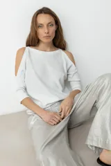 Sweater de tejido de punto fino con efecto lurex brillante, color plateado claro. Presenta un escote bote y aberturas en los hombros (cold shoulder) con mangas tres cuartos.
