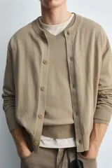 Cárdigan color beige de corte relaxed fit, tejido en hilatura con algodón y ramio. Tiene cuello redondo, manga larga, acabados en rib y cierre frontal de botonadura.
