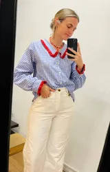 Camisa de algodón a cuadros azules y blancos con cuello y puños con volados rojos.