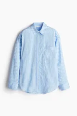 Camisa celeste y blanca a rayas verticales, de corte amplio, con cuello clásico, cierre frontal con botones, bolsillo de parche en el pecho, mangas largas con puños abotonados y bajo redondeado.