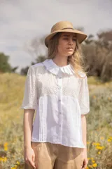Blusa blanca de lino con detalles de broderie de algodón, cuello babero y mangas cortas.