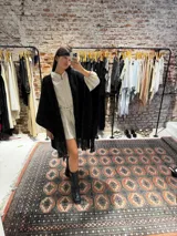 Ruana negra tejida a mano en lana merino con detalles de brillos y flecos.