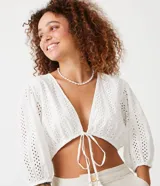 Blusa cropped blanca de laise texturizado con mangas 3/4 ajustadas y lazo en el bajo.