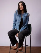 Campera de jean celeste de la marca Baccini, con cierre central, bolsillos delanteros, apliques colgantes de tachas en los hombros y terminación desflecada en el ruedo.