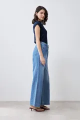 Pantalón de jean celeste de corte ancho, con cintura alta, pinzas y bolsillos laterales. Se ajusta a la cintura con un cinturón de cuero marrón.