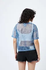 Top translúcido azul con estampado abstracto, de manga corta y tejido liviano con sutil brillo metálico.