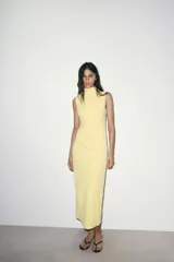 Vestido midi color blanco hueso, sin mangas, con cuello alto y detalle de drapeado fruncido en el lateral izquierdo del torso.