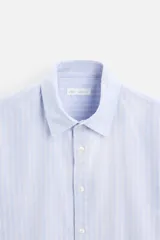 Camisa celeste con rayas verticales blancas, de corte regular, cuello solapa, manga larga con puños abotonados y cierre frontal con botones.