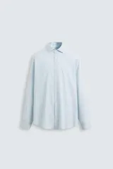 Camisa celeste a rayas verticales, de corte regular fit, con cuello italiano abierto, mangas largas con puños abotonados y cierre frontal con botones.