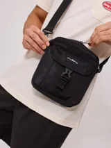 Bandolera gris de nylon con correa negra ajustable y logo Rusty estampado en negro.