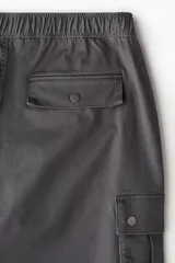 Pantalón cargo gris oscuro de corte holgado, con cintura elástica y bolsillos laterales, traseros y tipo cargo con solapa y botón a presión.
