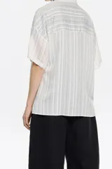 Camisa oversize blanca con rayas verticales finas en gris oscuro, cuello camisero, manga corta ancha, cierre frontal con botones y bolsillo de parche en el pecho. Confeccionada en viscosa y poliamida.