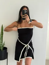 Vestido corto negro sin mangas, con escote recto con borde blanco y lazo blanco decorativo en la cintura.