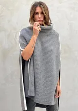 Poncho tejido de punto grueso color gris con cuello alto y aberturas laterales con ribete blanco.
