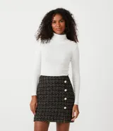 Blusa de tejido de punto acanalado color blanco, de manga larga y corte ajustado. Presenta cuello alto y detalles de botones dorados en los hombros.