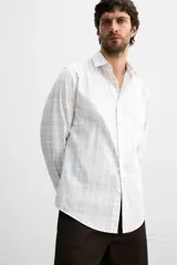Camisa de vestir slim fit de algodón, color blanco con diseño de cuadros en tonos grises y beige. Tiene cuello italiano, mangas largas con puños abotonados y cierre frontal con botones.