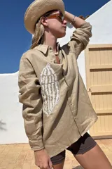 Camisa beige de lino con bordado de concha marina en el frente, de corte recto y mangas largas.