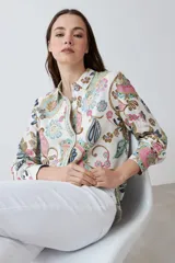 Camisa de manga larga con estampado de arabescos en tonos rosa, celeste, marrón y verde agua sobre fondo blanco. Tiene cuello clásico y cierre con botones.