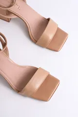 Sandalia de cuero color nude, con tira delgada sobre los dedos, pulsera al tobillo con hebilla y tacón cuadrado.