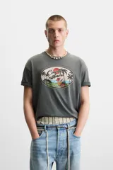 Camiseta gris de corte recto con cuello redondo y mangas cortas. Estampado ovalado con palmeras, sol y texto "Coconut Amora. Maui Offers Paradise".