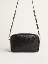 Bolso bandolera negro de cuero con efecto desgastado y estrella en relieve. Tiene correa de cuero ajustable y detalles metálicos dorados.