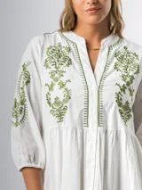 Vestido corto blanco de algodón italiano con bordado floral verde en el frente, mangas tres cuartos y botones en todo el largo. Tiene forro interior en la falda.