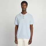 Remera tipo polo celeste de punto con cuello clásico y tres botones marrones.