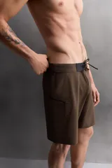 Bañador corto color marrón con cintura elástica negra ajustable con cordón. Tiene un bolsillo lateral con cierre de cremallera y costuras planas termofijadas.