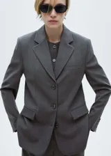 Blazer gris con estampado de raya diplomática, cuello con solapa, cierre de botones en la parte delantera, manga larga con puños abotonados, hombreras y dos bolsillos de solapa en la parte delantera.