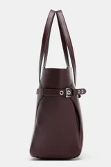 Bolso tipo shopper grande de cuero sintético color borgoña (vino tinto), con doble asa de mano y detalles de ojales metálicos plateados en los laterales. Incluye asa extraíble para llevar al hombro o cruzado.