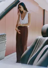 Pantalón de vestir de tiro medio, color marrón oscuro, con efecto arrugado en la tela satinada. Presenta un diseño recto, pinzas delanteras y cierre oculto.