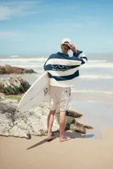 Buzo de tejido de punto grueso, estilo rugby, con cuello polo y tapeta de botones. Diseño a rayas horizontales anchas en blanco y azul marino, con bordes deshilachados en las uniones de las franjas. Presenta un logo bordado en el pecho.