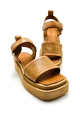 Sandalia de cuero vacuno color camel con plataforma corrida. La capellada ajusta en el empeine con sistema de velcro y tiene un tirador decorativo en el talón.
