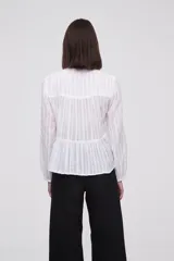 Blusa blanca con rayas verticales, cuello con lazo, mangas largas y corte holgado.