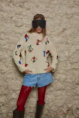 Sweater de lana color crema, tejido a mano con cuello redondo y mangas largas con trenzas. Presenta bordados de figuras esquiando.