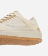 Championes casuales de caña baja, color beige y crema, con suela tipo caja. Presentan una combinación de materiales lisos y gamuza sintética, perforaciones en la punta para ventilación, cierre de cordones y punta redondeada.