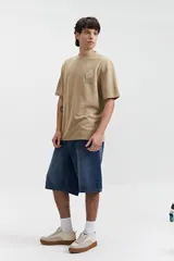 Remera beige de manga corta con textura y corte oversize. Presenta un pequeño bordado en relieve en el pecho.