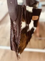 Bolso maxi de cuero con estampado de vaca en blanco y negro, y cuero color chocolate en la parte posterior. Tiene correa larga para colgar al hombro.