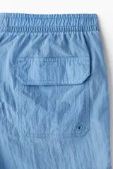 Short de baño azul de nylon con elástico revestido y cordón para ajustar oculto en la cintura, bolsillos laterales y bolsillo de solapa con cierre autoadherente atrás. Largo por encima de la rodilla con abertura corta en los laterales y suspensor interior en malla suave.