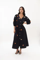 Vestido midi color arena con escote en V, mangas 3/4 abullonadas y cierre frontal con botones. Presenta bordados de motivos marinos.