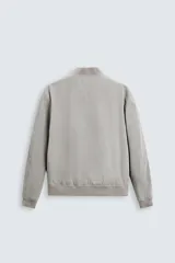 Cazadora bomber ligera gris confeccionada en tejido técnico. Cuello y puños en rib elástico, manga larga, bolsillos de vivo en cadera y bolsillo interior. Cierre frontal con cremallera.