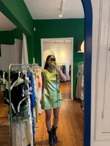 Vestido corto color verde lima con estampado floral blanco, corte cheongsam, cuello mao, sin mangas, con ribete negro y lazos decorativos en el lateral.