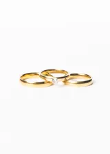 Set de tres anillos dorados, dos alianzas lisas y un cintillo con una piedra engarzada, presentados en un estuche blanco.
